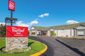 Un hotel Red Roof Inn con cielo despejado, entrada de piedra y estacionamiento.