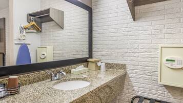 Un baño con encimera de granito, un lavamanos, un espejo, dispensador de toallas y teclado de seguridad.