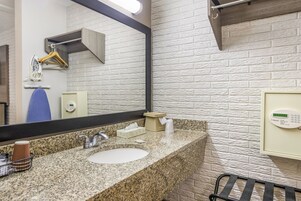 Un baño con encimera de granito, un lavamanos, un espejo, dispensador de toallas y teclado de seguridad.
