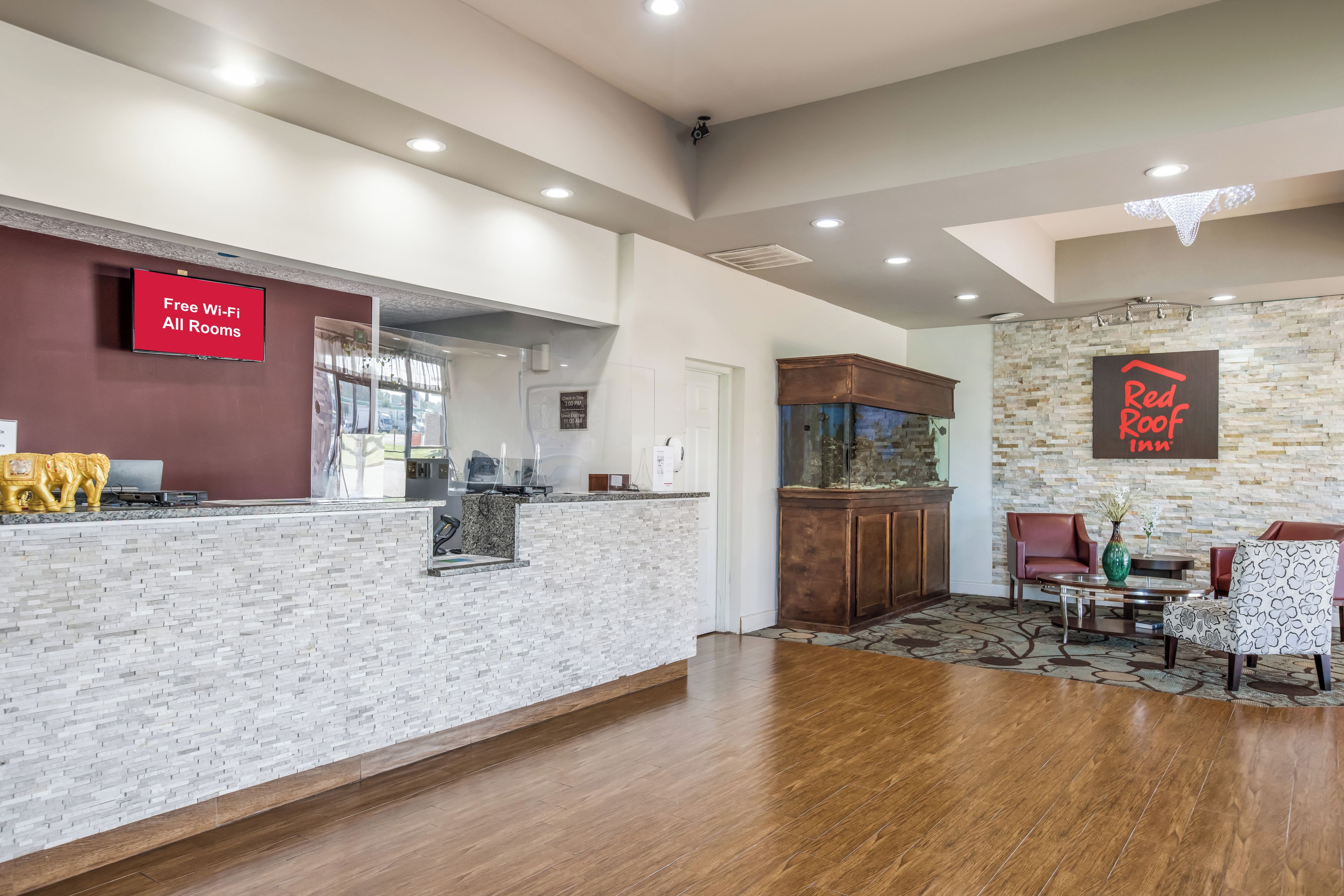 A hotel lobby with a reception desk, a Red Roof Inn sign, a fish tank, and a seating area with a patterned rug.