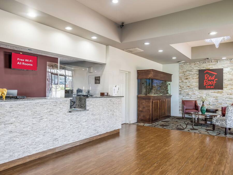 A hotel lobby with a reception desk, a Red Roof Inn sign, a fish tank, and a seating area with a patterned rug.