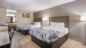 Habitación de hotel con dos camas, un escritorio, una silla, un espejo y un cuadro en la pared.