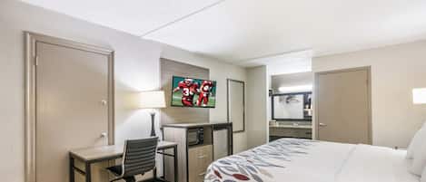 A hotel room with a bed, desk, chair, television, and a bathroom visible through an open door.