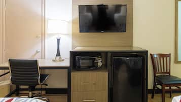 A hotel room with a bed, a desk with a chair, a television mounted on the wall, a microwave, and a refrigerator.