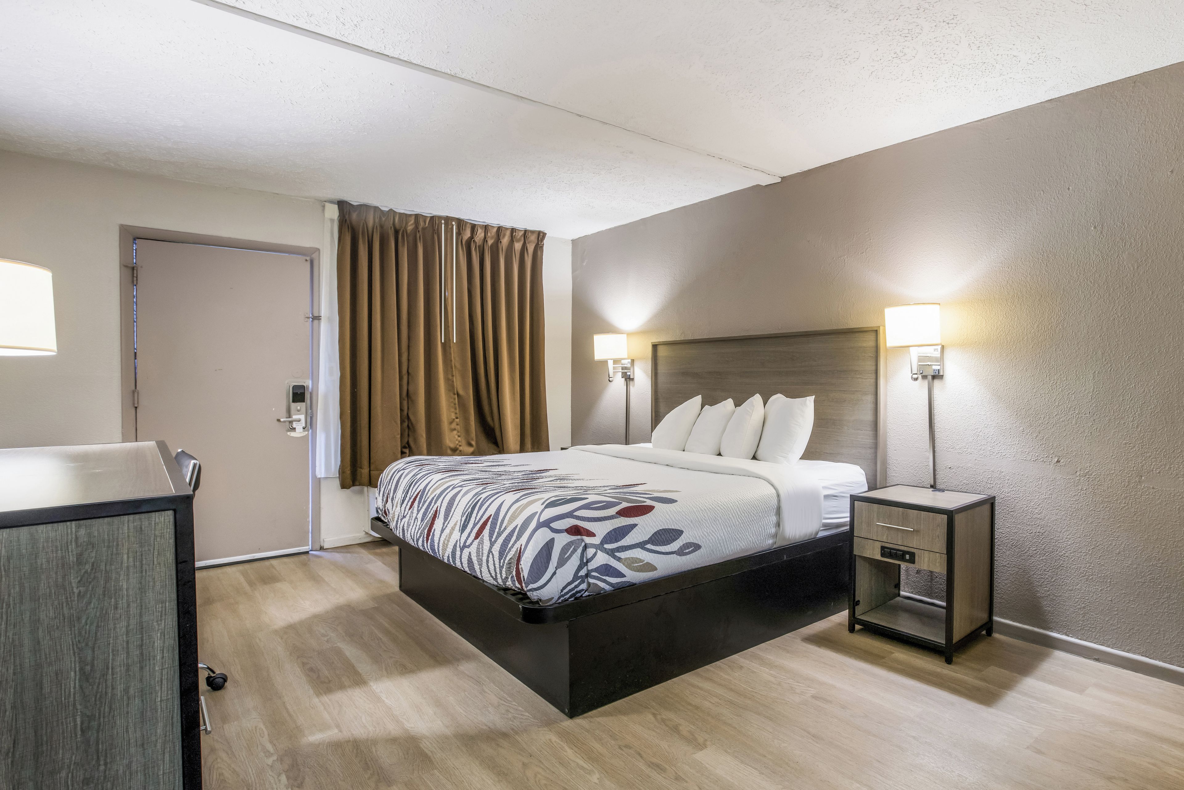 A hotel room with a bed, bedside tables, a desk, and a door.