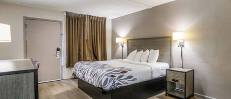 A hotel room with a bed, bedside tables, a desk, and a door.