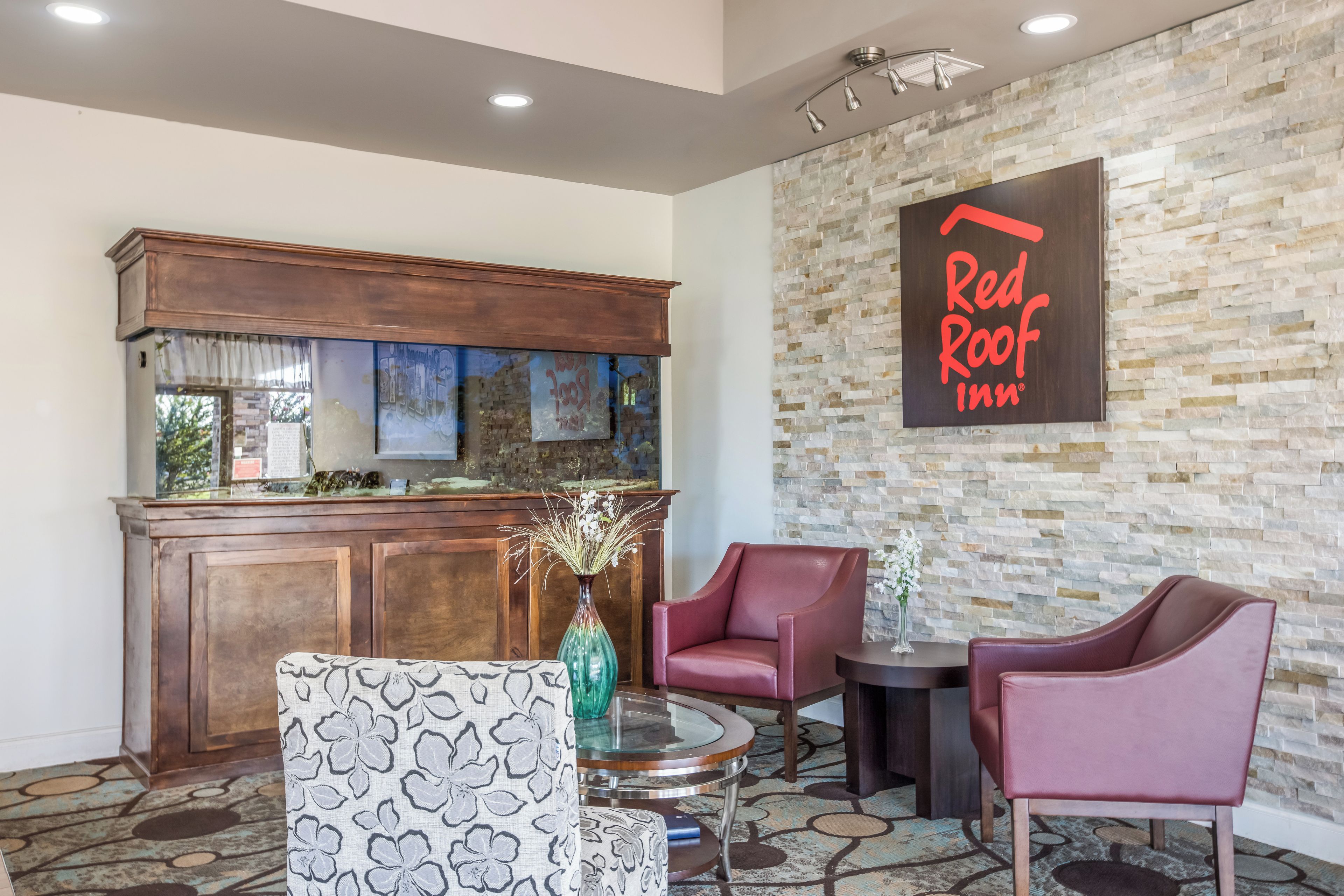 Un hall d’entrée de Red Roof Inn avec un mur en pierre, un bar en bois et un espace salon.