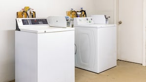 Deux machines à laver à chargement frontal, de couleur blanche, se trouvent dans une buanderie. On peut voir les panneaux de commande et les tuyaux.