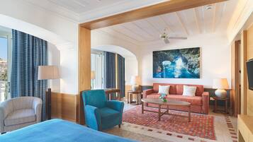 Una habitación de hotel con una cama, un sillón azul, un sofá rojo, una mesita de café y un cuadro en la pared.