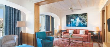 Una habitación de hotel con una cama, un sillón azul, un sofá rojo, una mesita de café y un cuadro en la pared.