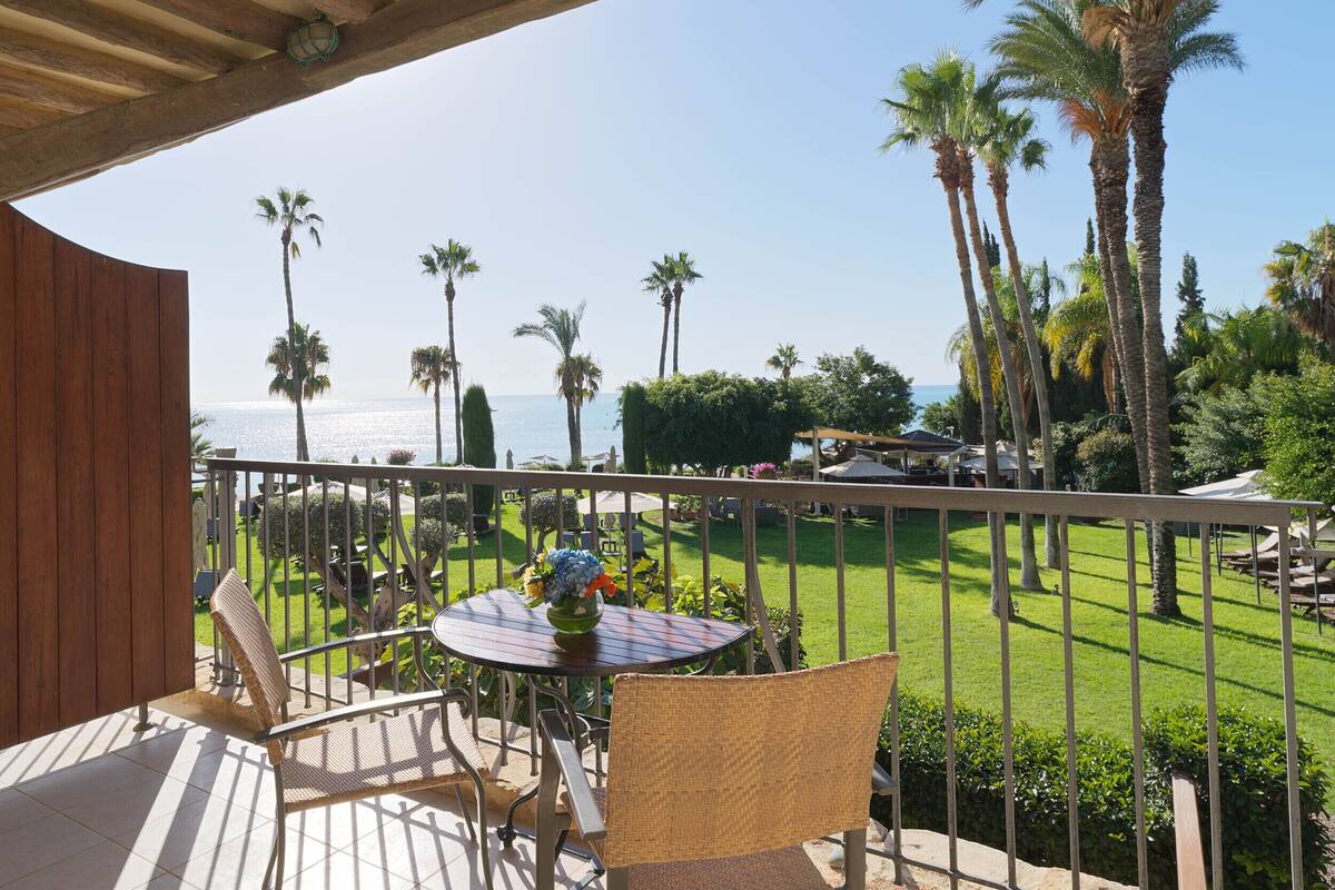 A balcony with a view of the ocean, palm trees, and a well-maintained lawn.