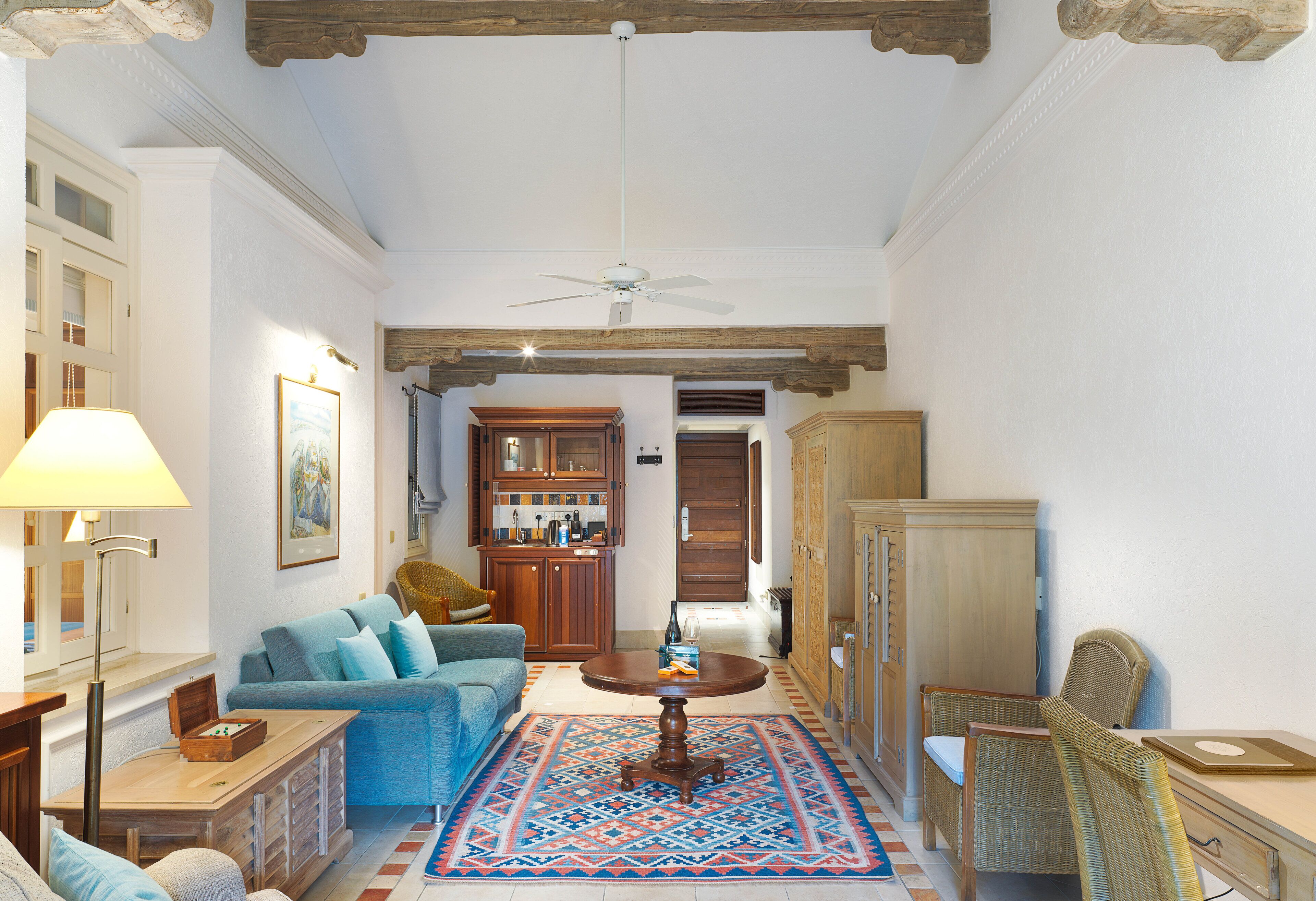A living room with a blue sofa, wooden cabinets, a dining table, and a patterned rug.