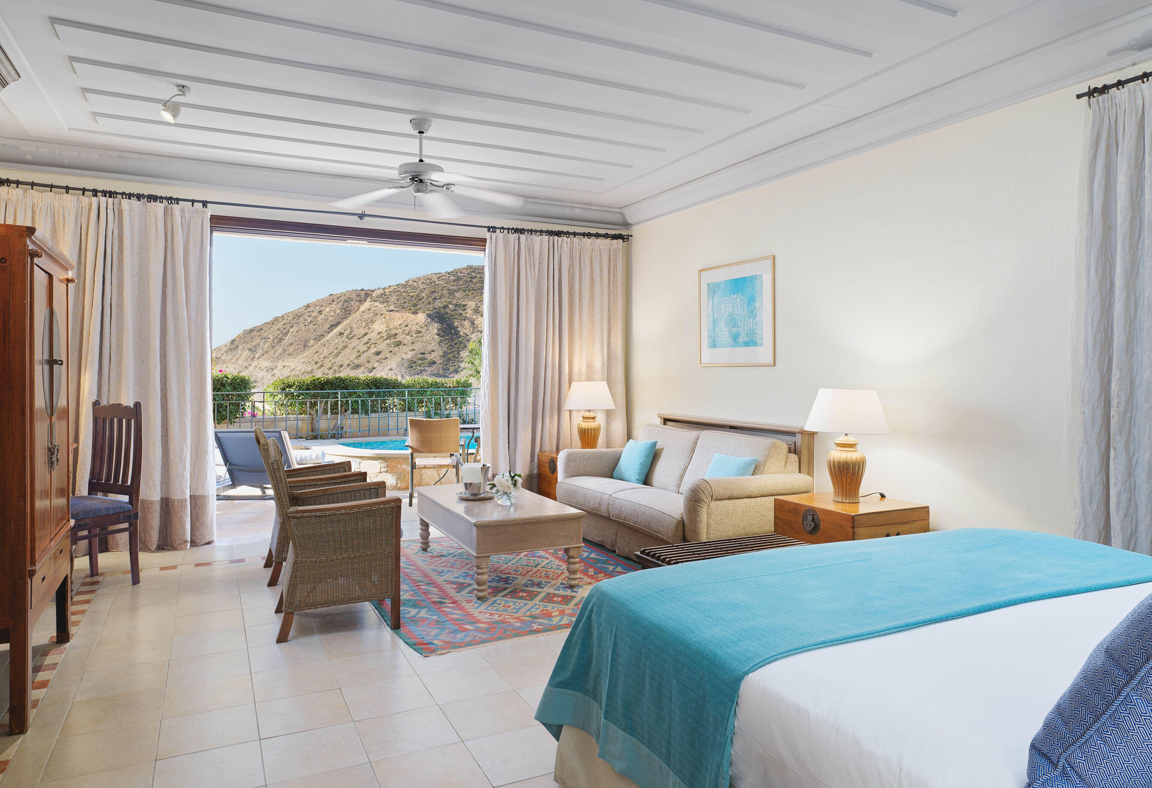 A hotel room with a bed, a sofa, a chair, a desk, and a view of a mountain.