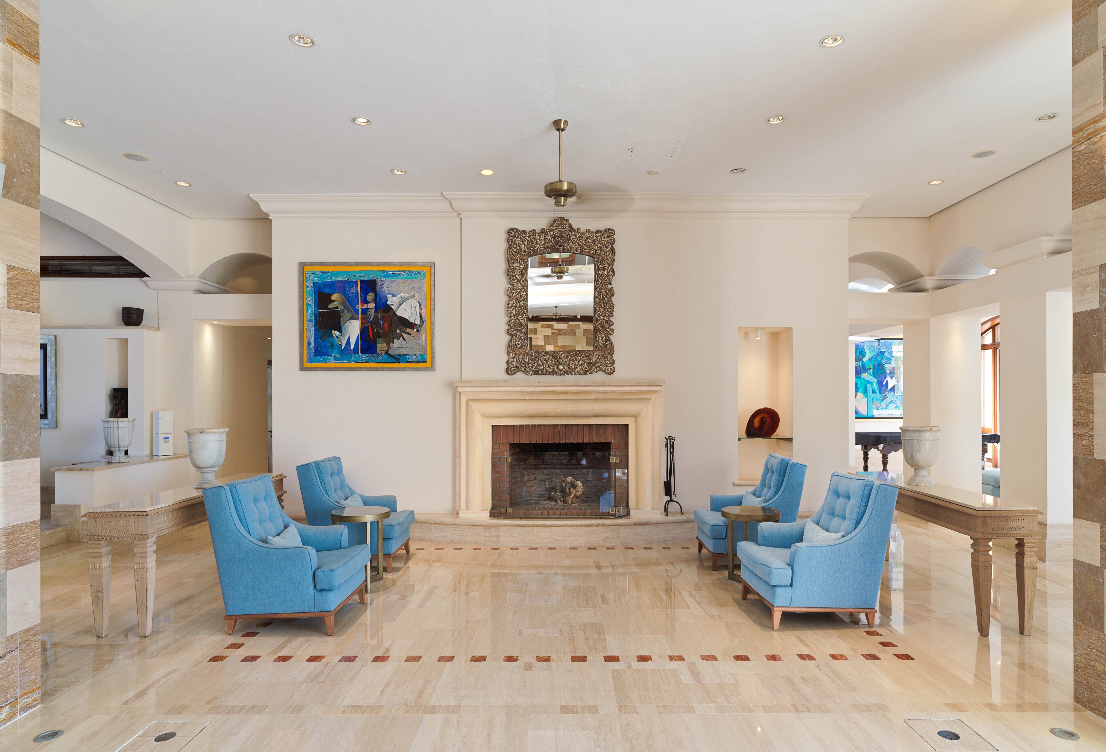 A spacious lobby with a fireplace, blue armchairs, and a large mirror.