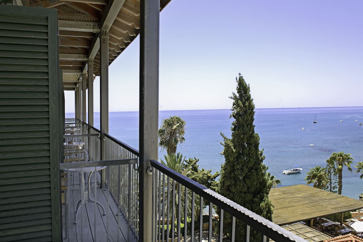A balcony with a view of the sea, featuring a wooden deck and metal railing.