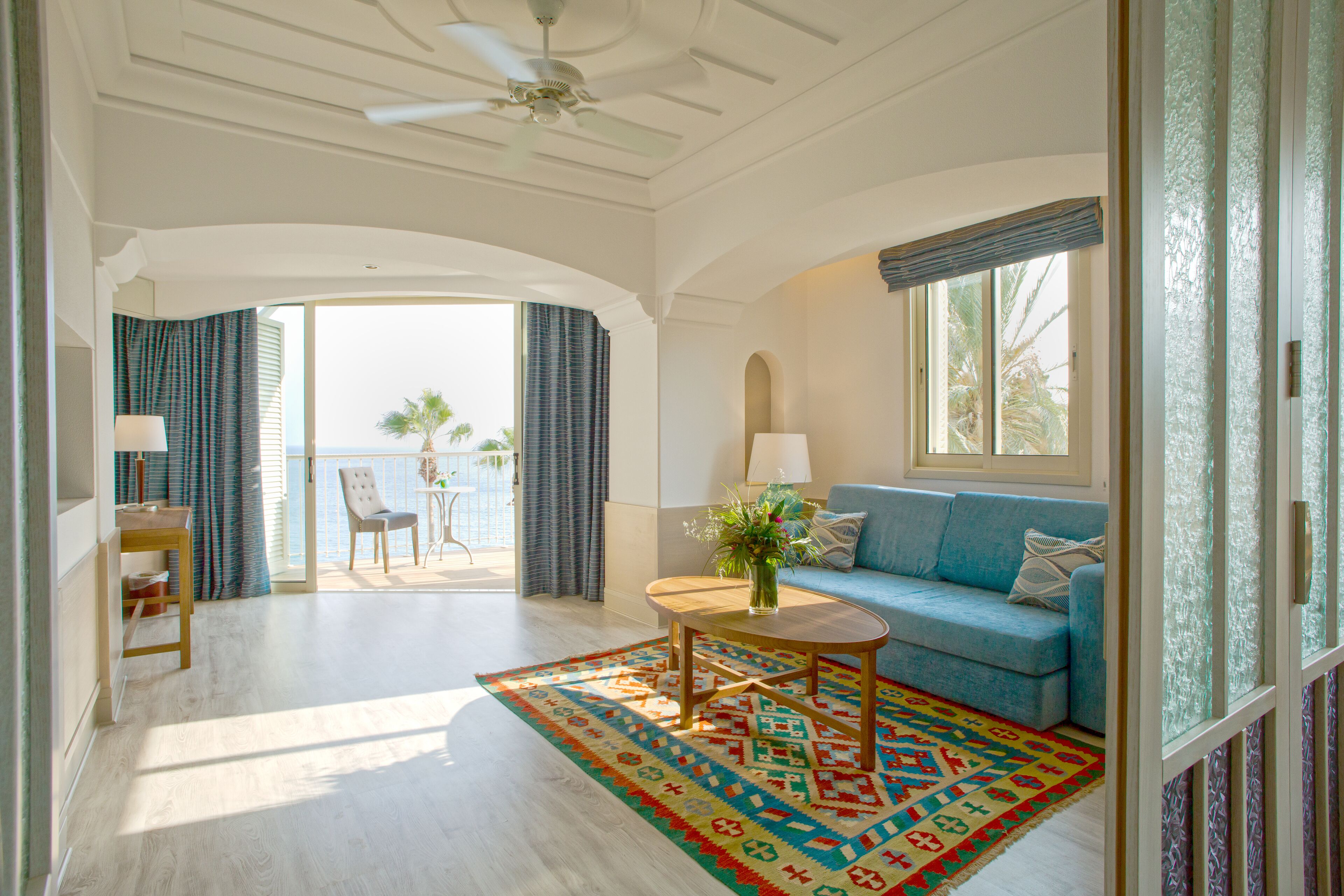A spacious living room with a blue sofa, a wooden coffee table, and a patterned rug.