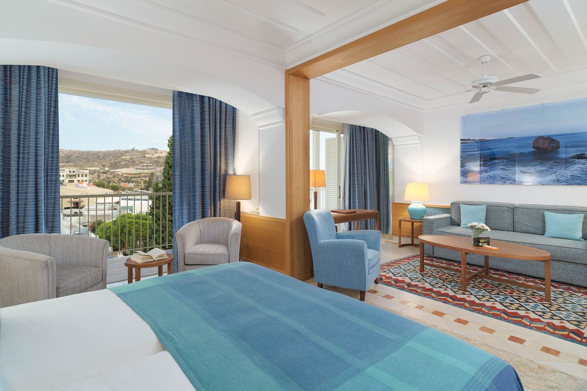 Une chambre d’hôtel comprenant un lit, deux fauteuils, un canapé, une petite table et une vue sur la mer.