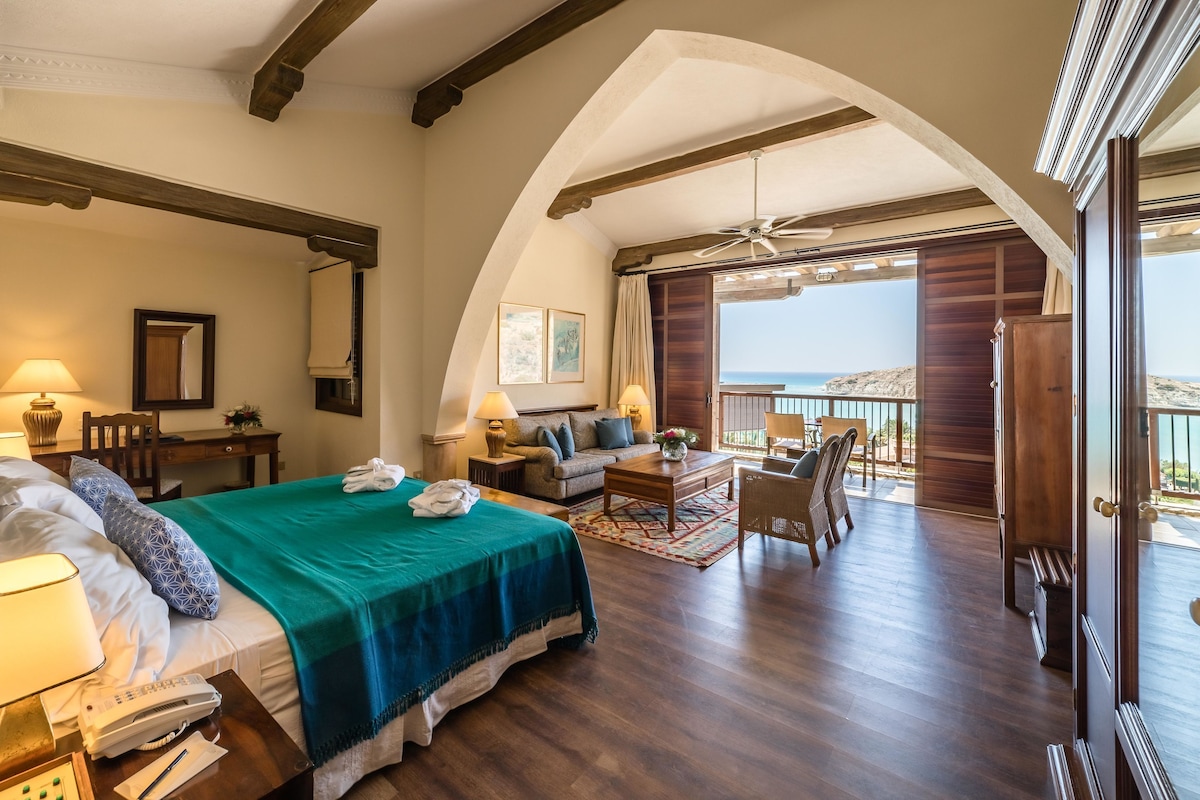 Une chambre spacieuse avec un grand lit, un bureau, une chaise et un balcon offrant une vue sur la mer.