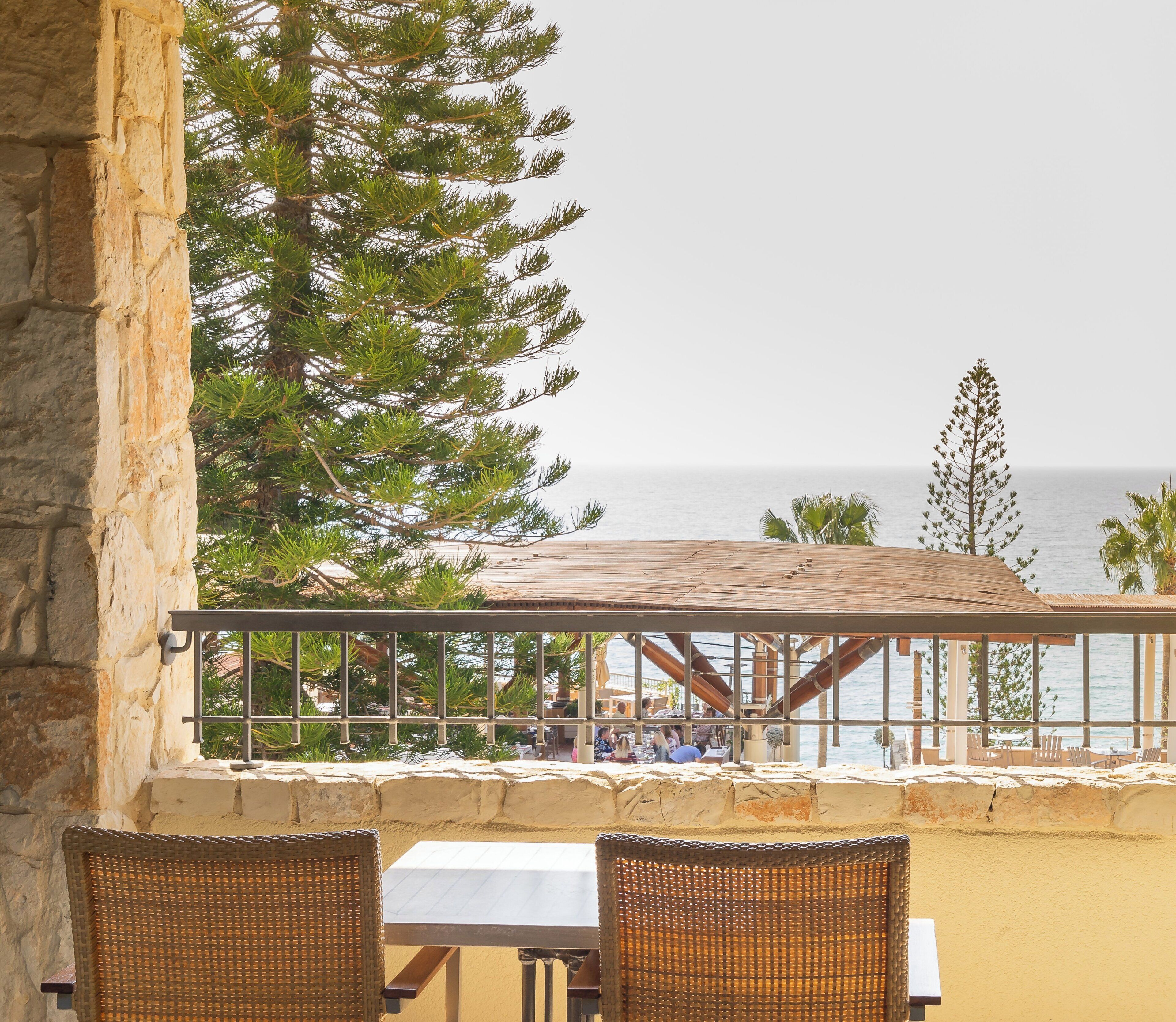 An outdoor seating area with a view of the sea, stone walls, and a wooden pergola.