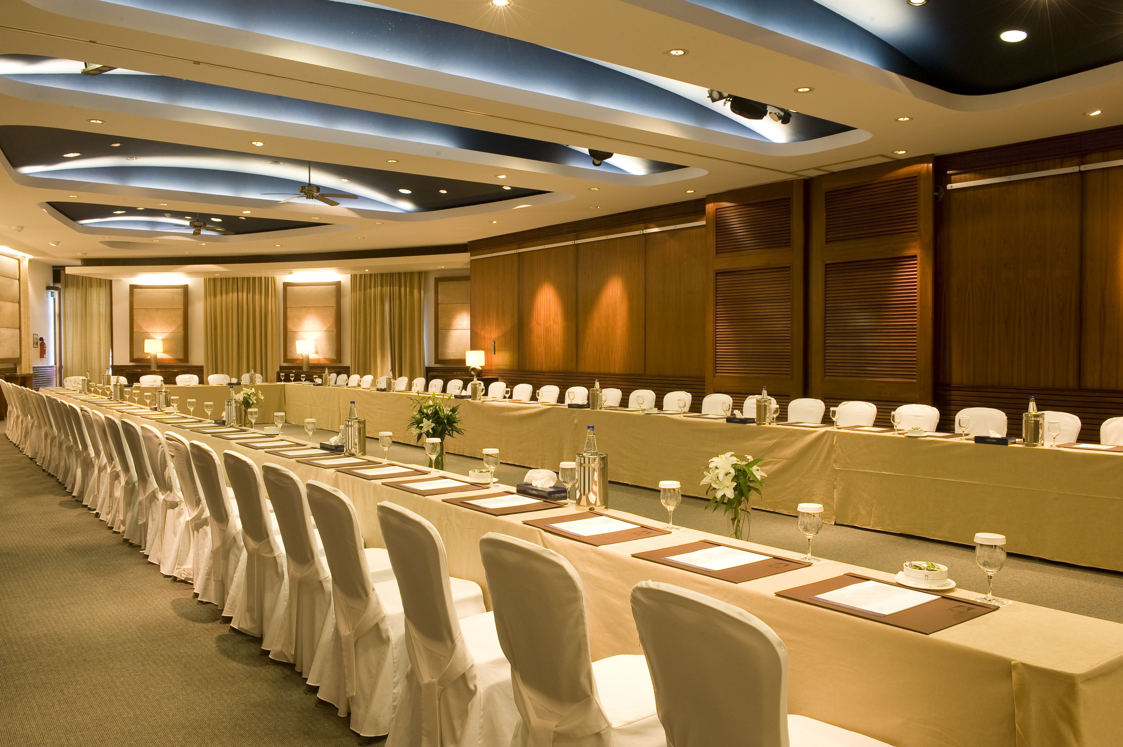 A conference room with a long table, white chairs, and a ceiling with recessed lighting.