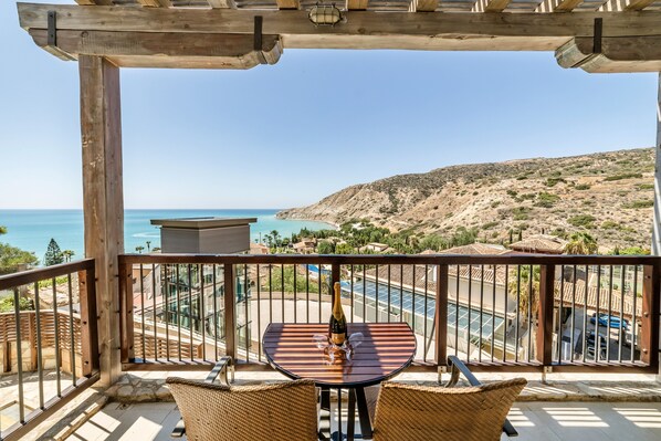A balcony with a table and chairs, overlooking a pool and a mountainous landscape. - Columbia Beach Resort (Pissouri)