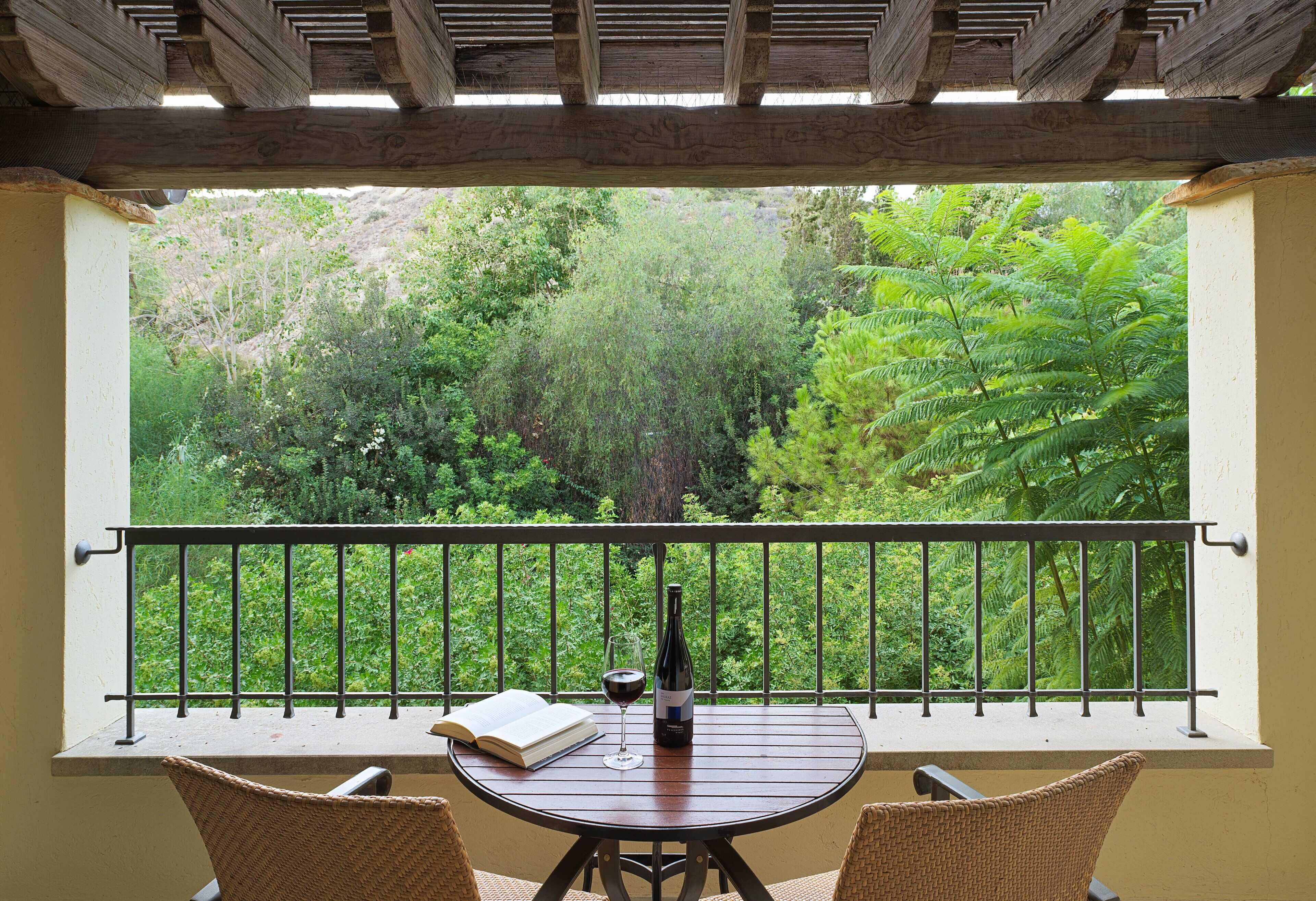 A balcony with a table, chairs, a book, and a bottle of wine.