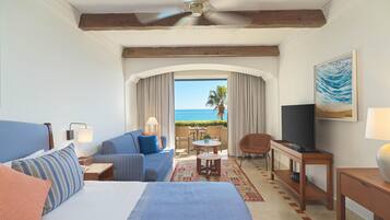 A hotel room with a bed, a sofa, a TV, a desk, and a view of the ocean.