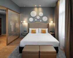 Quarto de hotel moderno com uma cama grande, duas mesas de cabeceira, uma luminária fixada na parede e pratos decorativos.