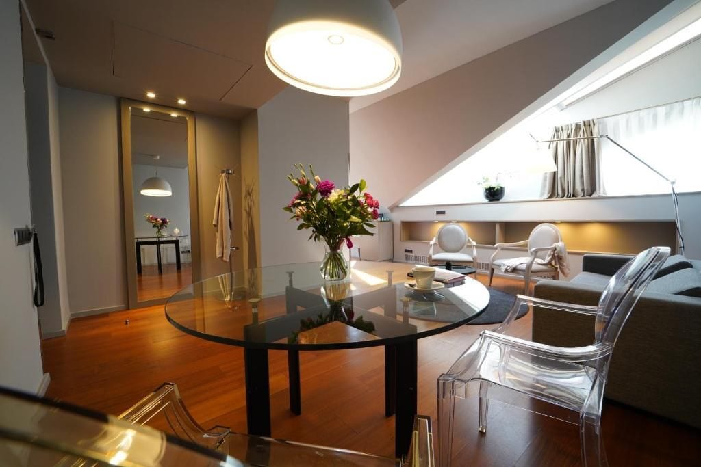 A modern living room with a glass table, clear chairs, a sofa, and a large window.
