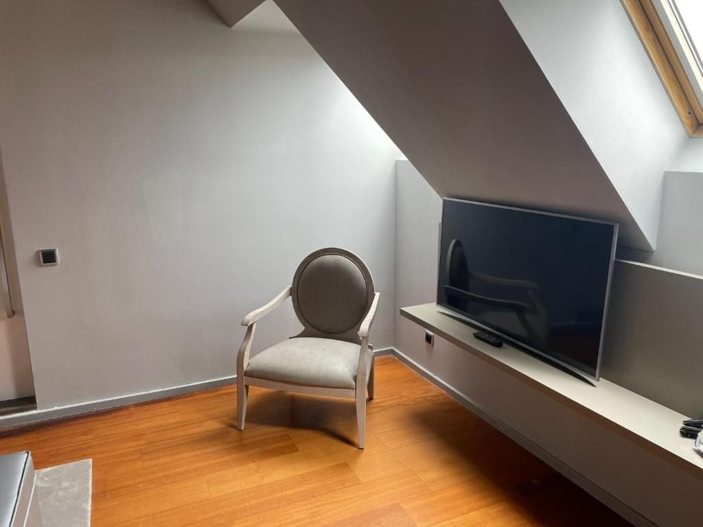 Ein modernes Wohnzimmer mit einem Flachbildfernseher, einem grauen Sessel und Holzboden.