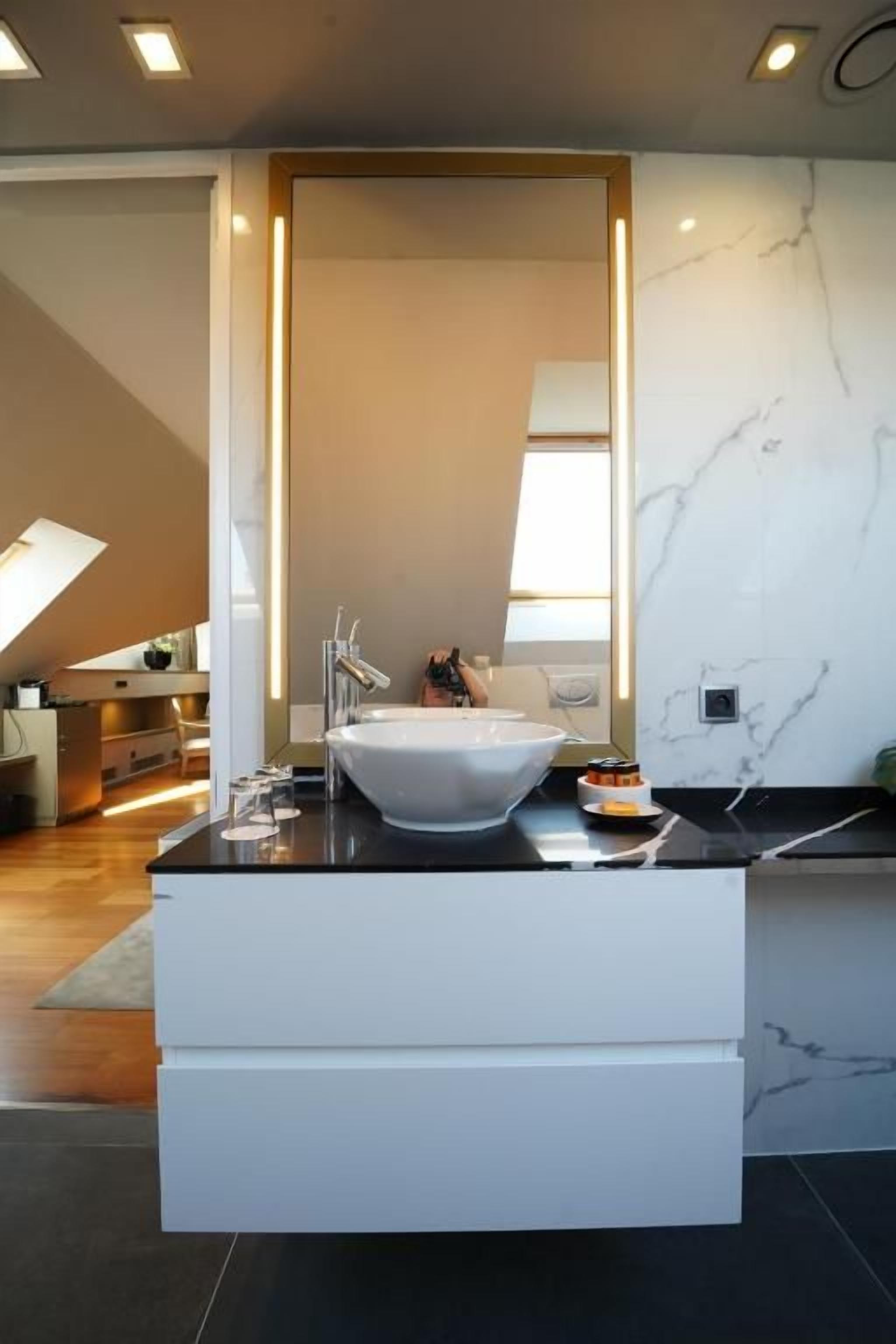 A modern bathroom with a large white sink, a mirror, and a marble wall.