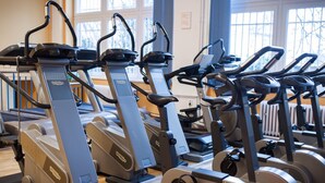 Une rangée de vélos d’appartement dans une salle de sport, avec de grandes fenêtres en arrière-plan.