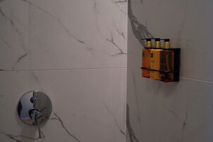 Casa de banho com parede de mármore, chuveiro com torneira cromada e um armário com produtos de higiene.