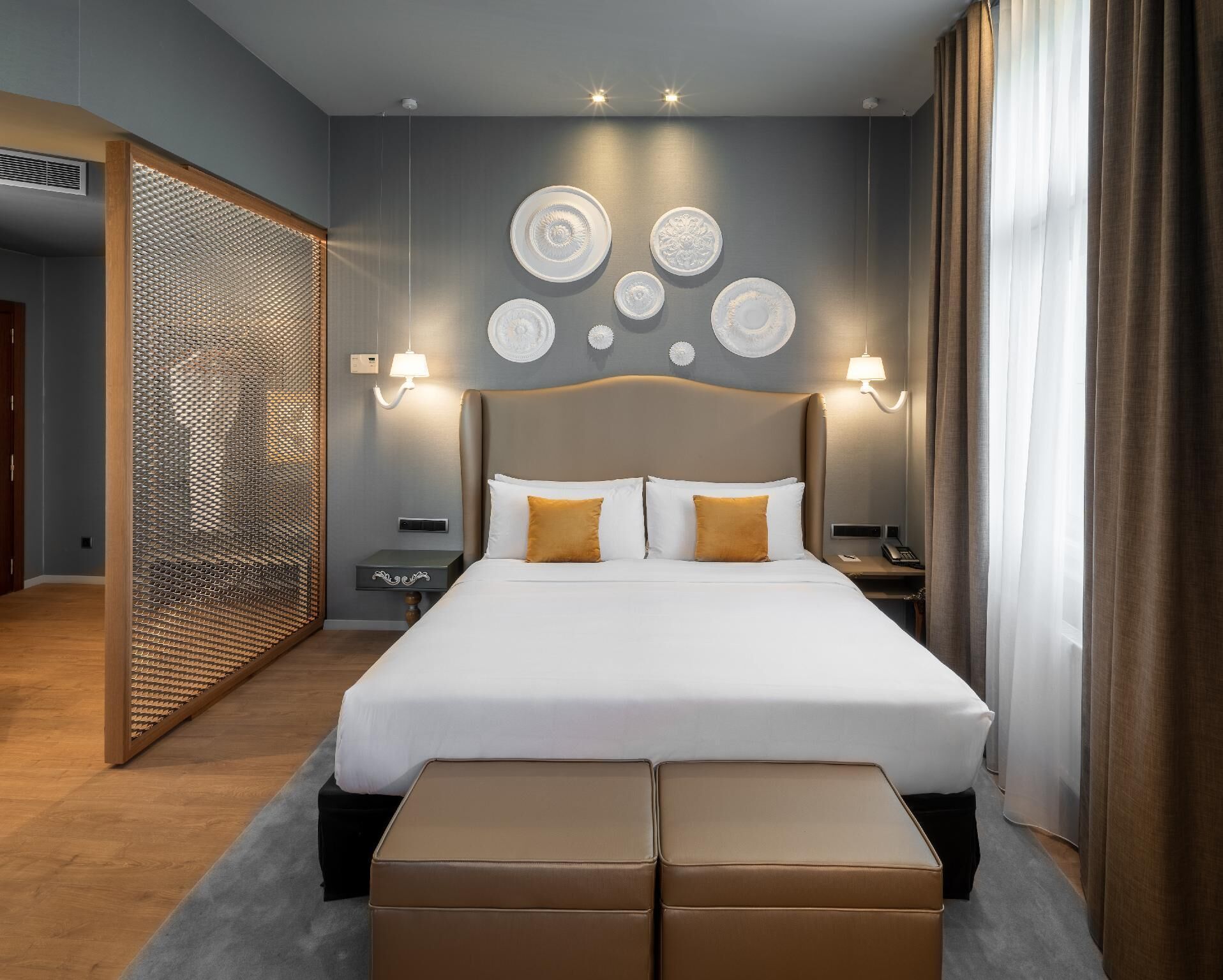 A modern hotel room with a large bed, two bedside tables, a wall-mounted lamp, and a decorative wall panel.