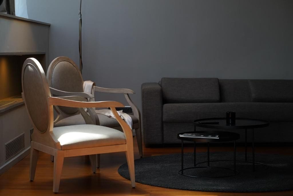 A room with a grey sofa, a wooden chair, and a small black table.