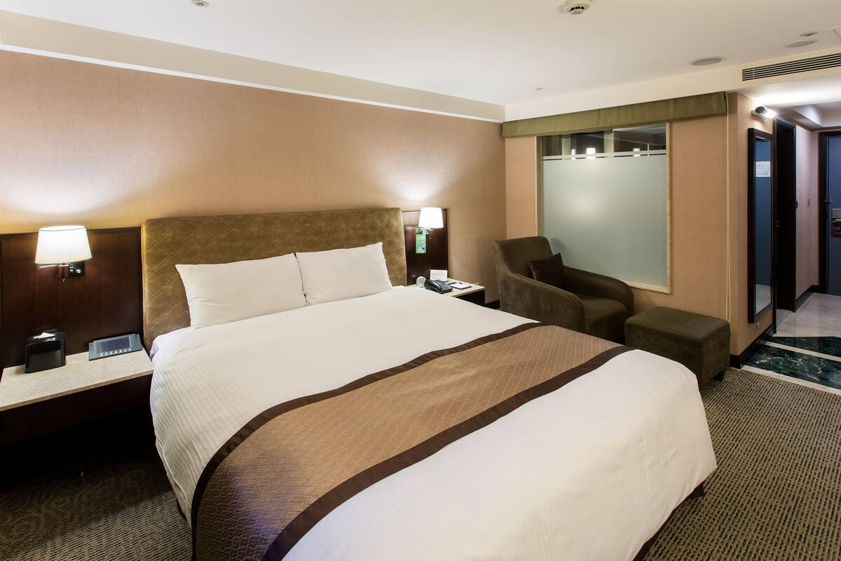 Une chambre d’hôtel avec un grand lit, un bureau avec une lampe, une chaise et un miroir.