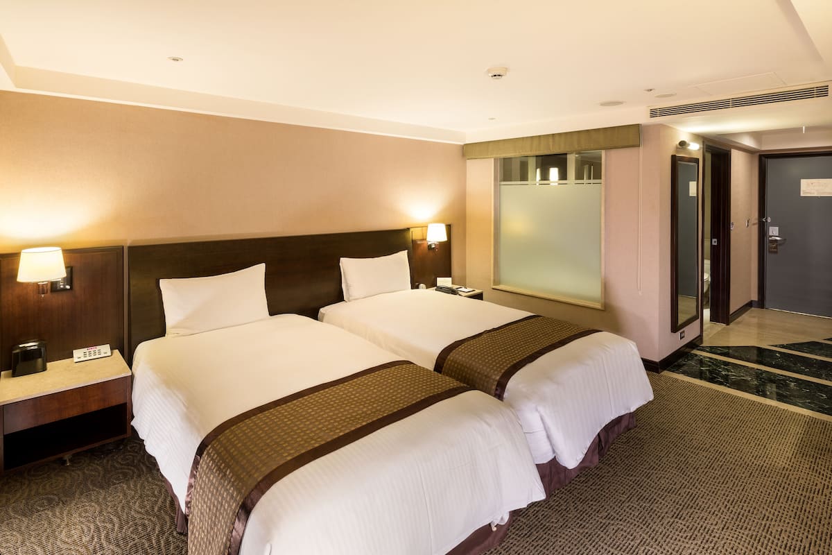 Une chambre d’hôtel avec deux lits, une table de chevet, une lampe, un miroir et une porte.