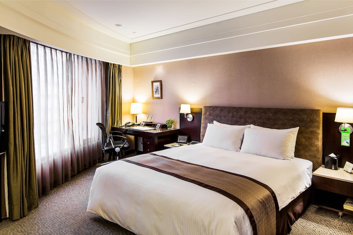 Une chambre d’hôtel avec un grand lit, un bureau avec un ordinateur, une chaise et une table de chevet avec une lampe.