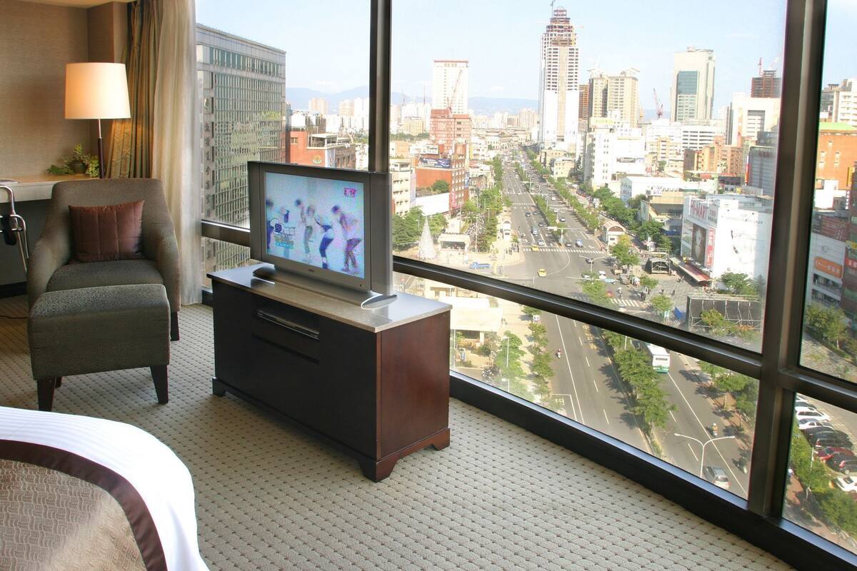 Une chambre d’hôtel avec une grande fenêtre, une télévision, une chaise et une petite table.