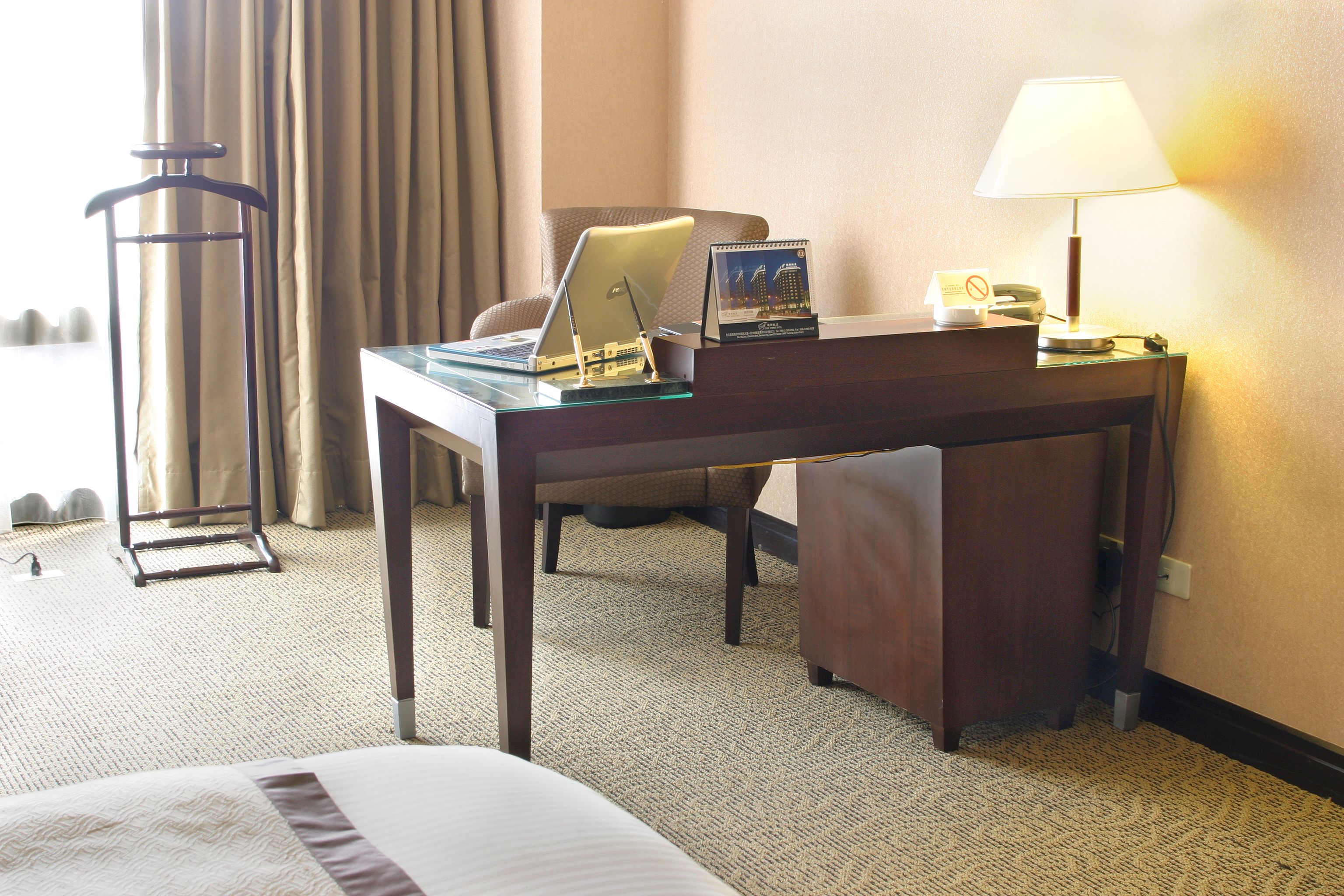 A hotel room with a bed, a desk with a laptop, a lamp, and a chair.