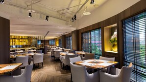 A modern restaurant with multiple dining tables and chairs, large windows with blinds, and a visible kitchen area in the background. - Grand Forward Hotel (New Taipei City)