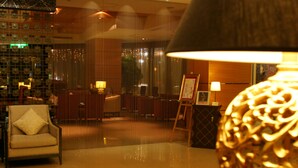 A lobby with a plush armchair, a standing lamp, and a framed artwork on a stand. - Grand Forward Hotel (New Taipei City)