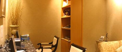 A room with a marble desk, two chairs, a bookshelf, a lamp, and a sofa.
