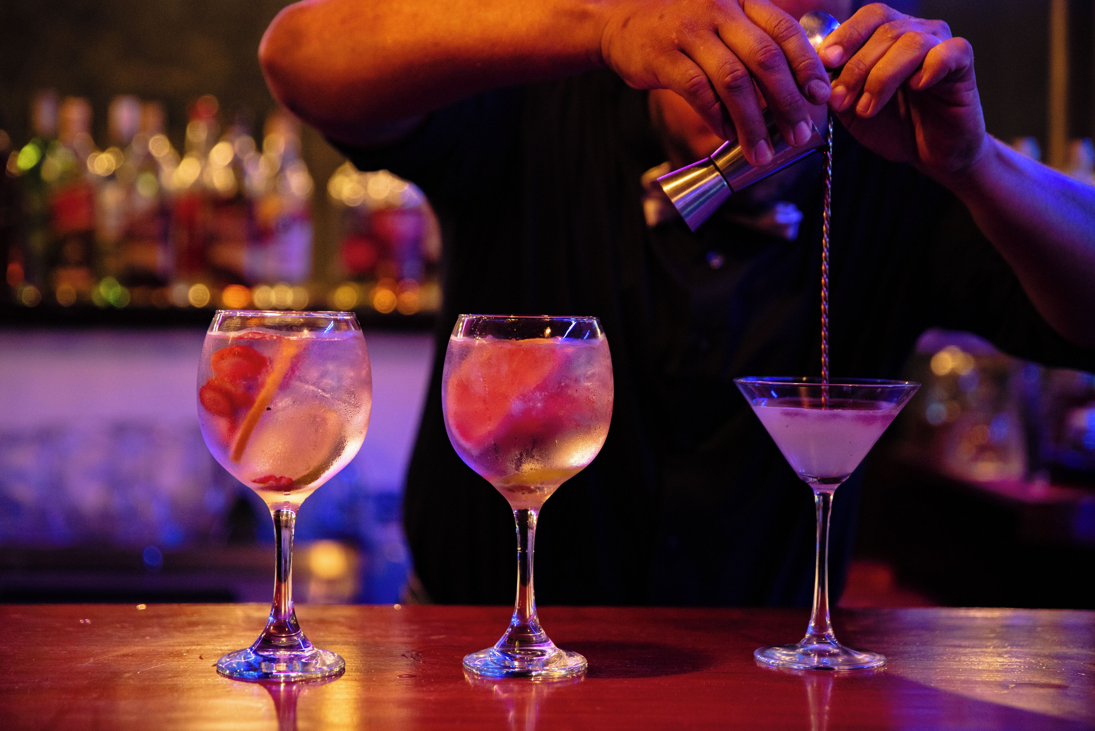 Three glasses of a clear, possibly alcoholic beverage with ice cubes on a bar counter.