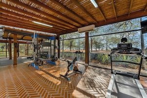 A gym with exercise equipment, a herringbone-patterned floor, and large windows offering a view of trees.