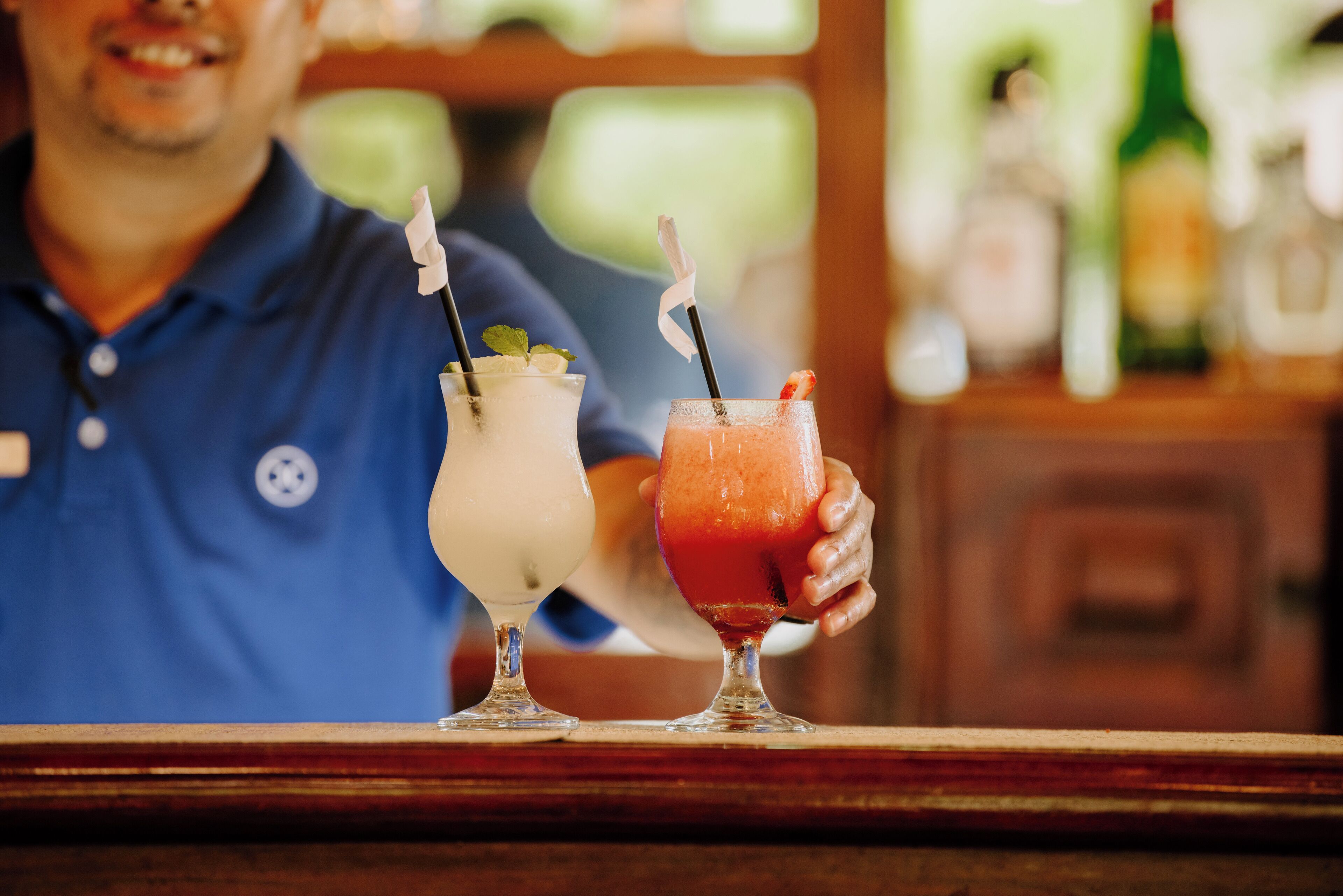 A bar setting with two drinks in glasses, one white and one red, with straws and garnishes.