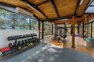 Un gimnasio con equipo de ejercicio, estantes para pesas y vistas a árboles y cielo.
