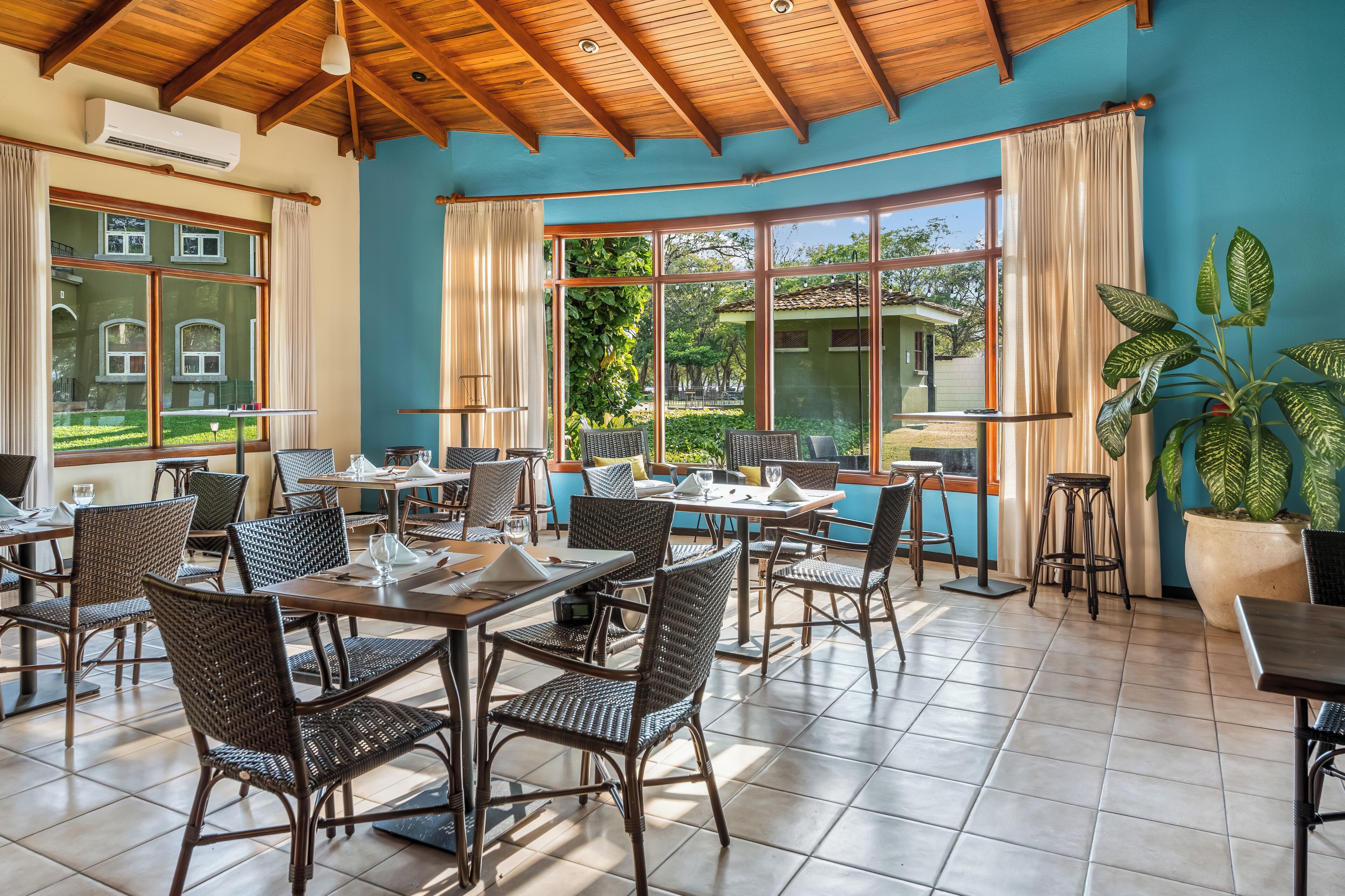 Un restaurante con terraza, grandes ventanales y vistas al jardín.