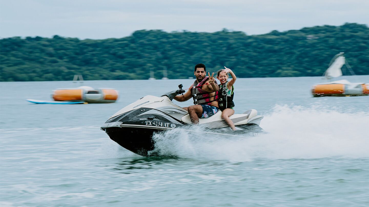 A person riding a jet ski on a body of water with buoys and a forested island in the background.