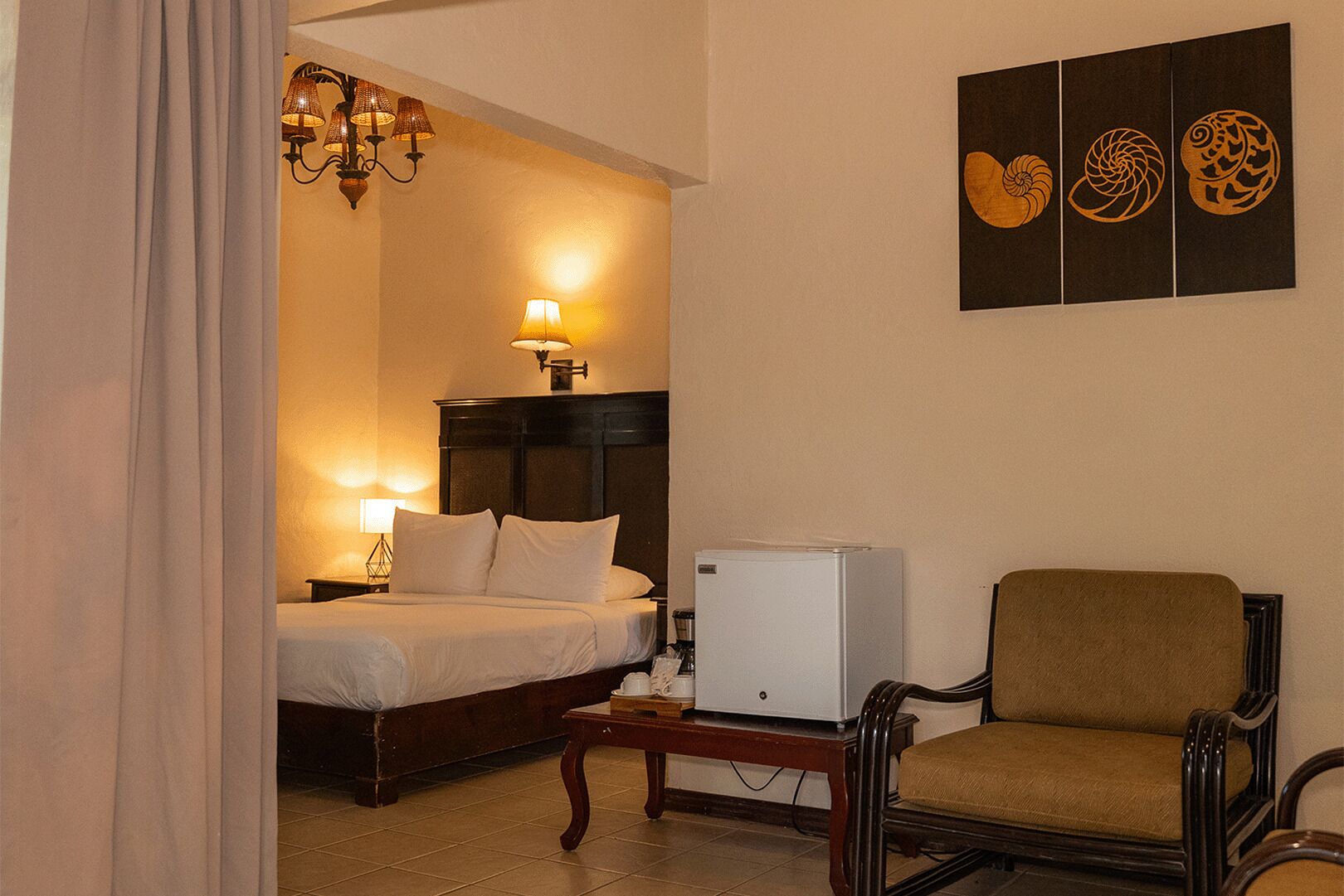 Une chambre d’hôtel avec un lit, une petite table, une chaise, un réfrigérateur et des œuvres d’art murales.